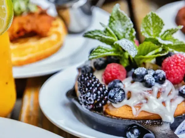 A cinnamon roll in a small skillet with icing, berries and mint, on a brunch table at Loreley