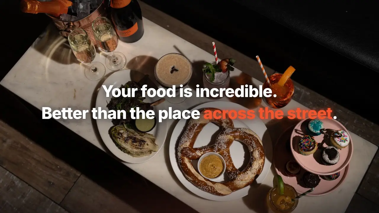 An overhead frame from a Tableify video: shared plates, a pretzel, cupcakes and cocktails on a marble table, with the words Your food is incredible. Better than the place across the street.
